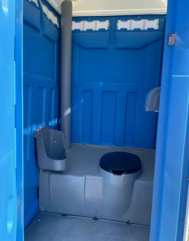 Clean interior of a blue standard porta potty with seat, urinal and vent pipe