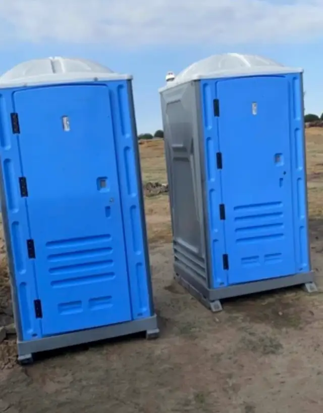 Blue and gray porta potties set on a dirt construction lot