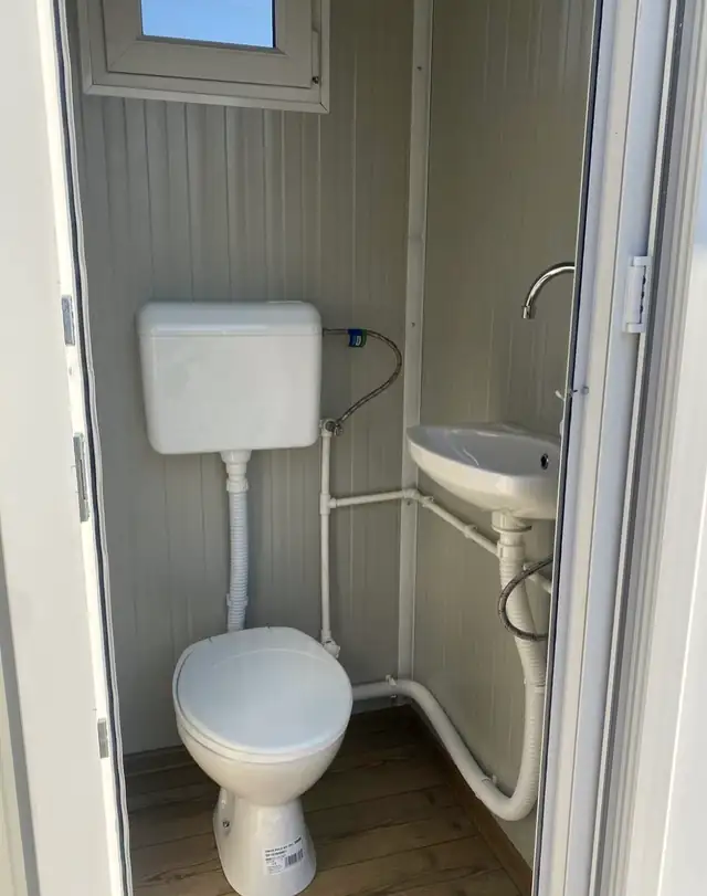 Flushing restroom cabin interior with tank toilet and wall sink