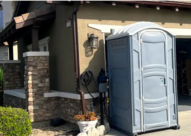 Gray porta potty set on a driveway beside a house remodel