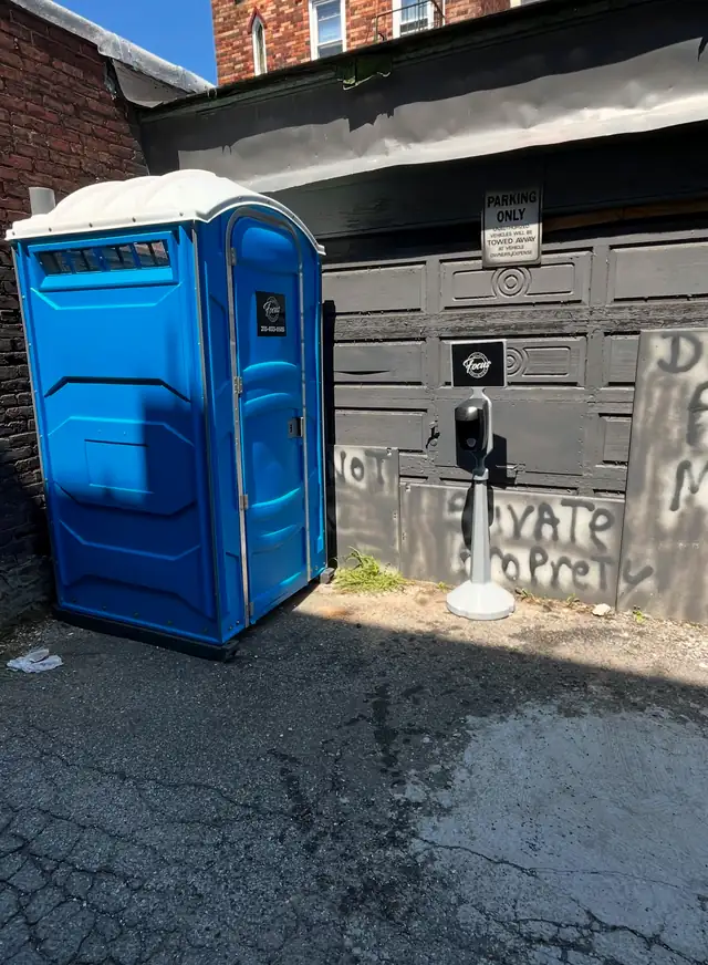 Blue porta potty placed off the pavement beside a garage