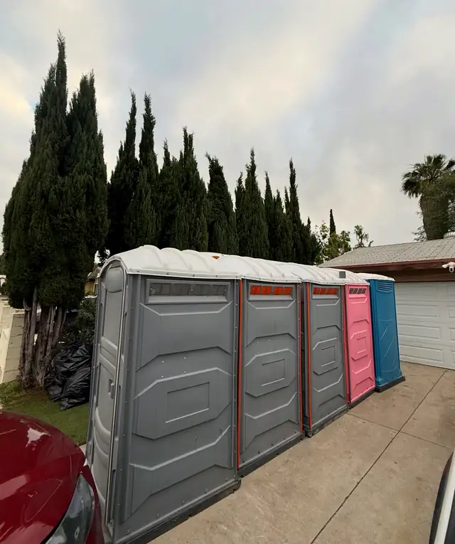 Row of gray, pink and blue porta potties along a residential street