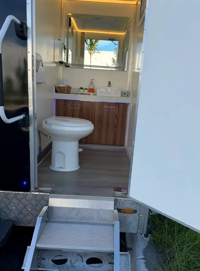 Restroom trailer stall with flushing toilet, wood vanity and lighting